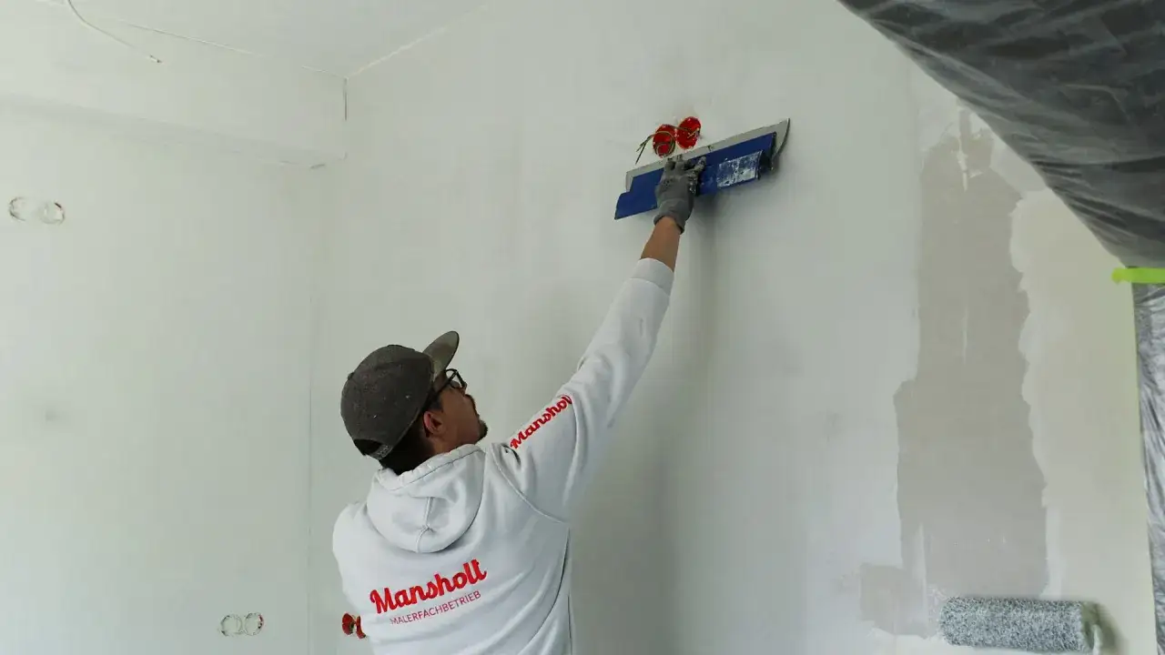 Maler mit Spachtel und Rolle bereitet Wand f&uuml;r q4 Spachtelung vor.