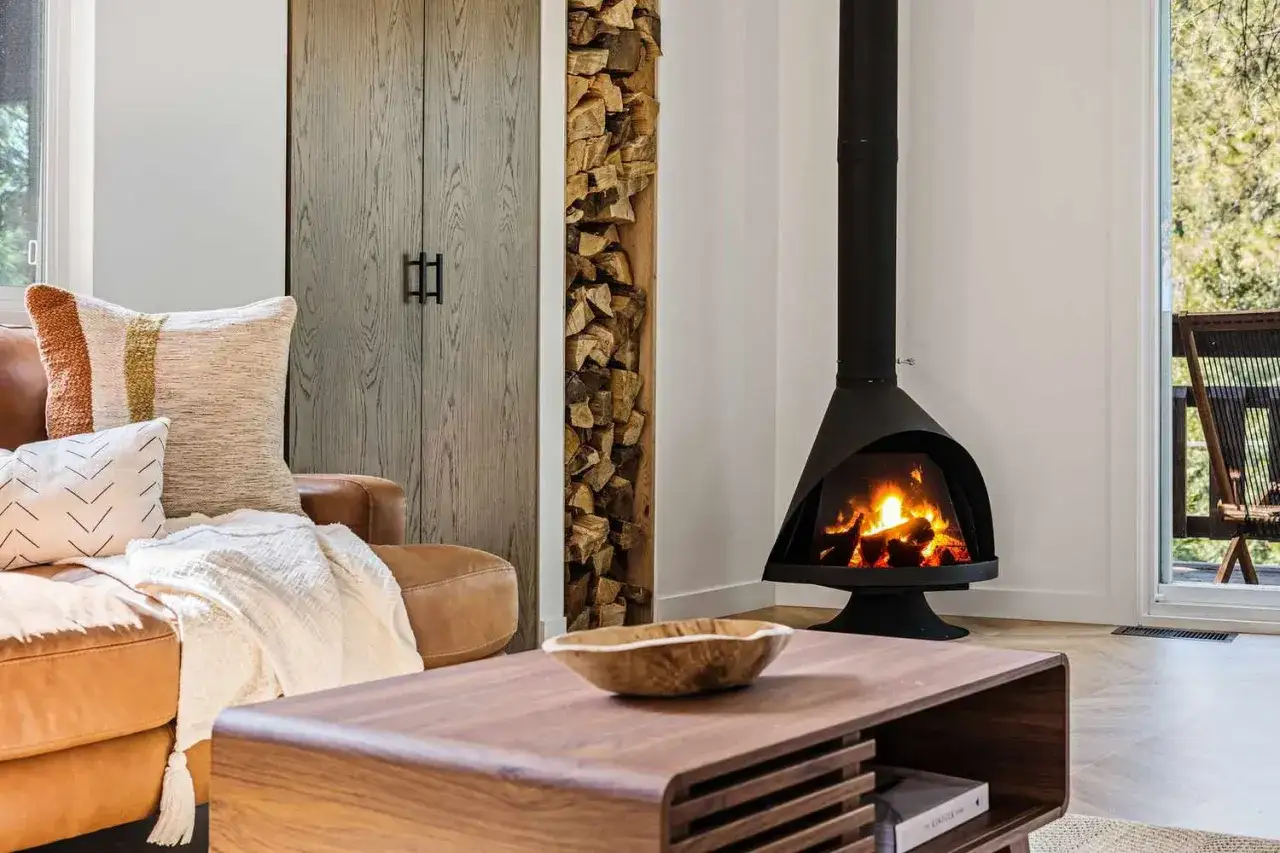 Gem&uuml;tliches Wohnzimmer mit Kaminfeuer und Holzstapel. Eine moderne Pellet-Hybridheizung sorgt f&uuml;r wohlige W&auml;rme.