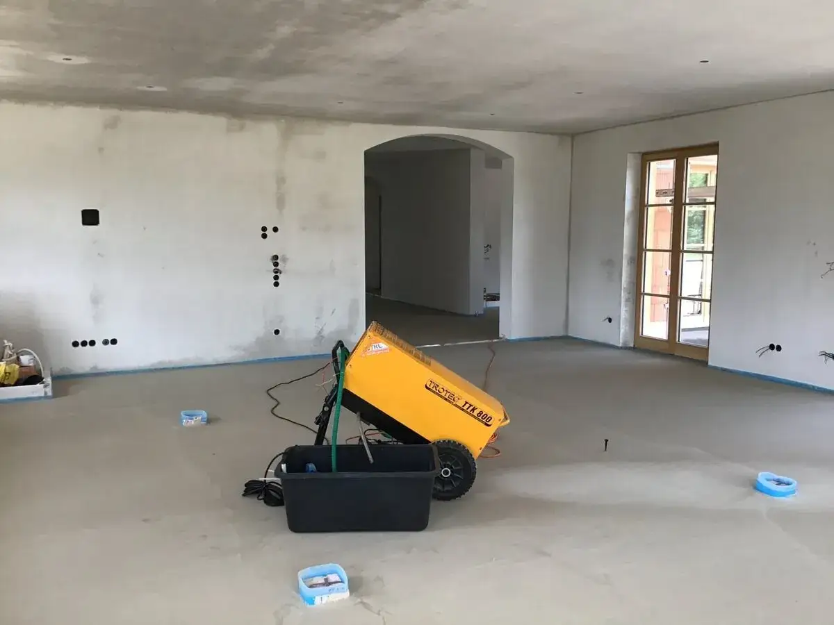 Ein gelber Bautrockner steht in einem Rohbau, um den Estrich zu trocknen. Der Raum ist noch unm&ouml;bliert.