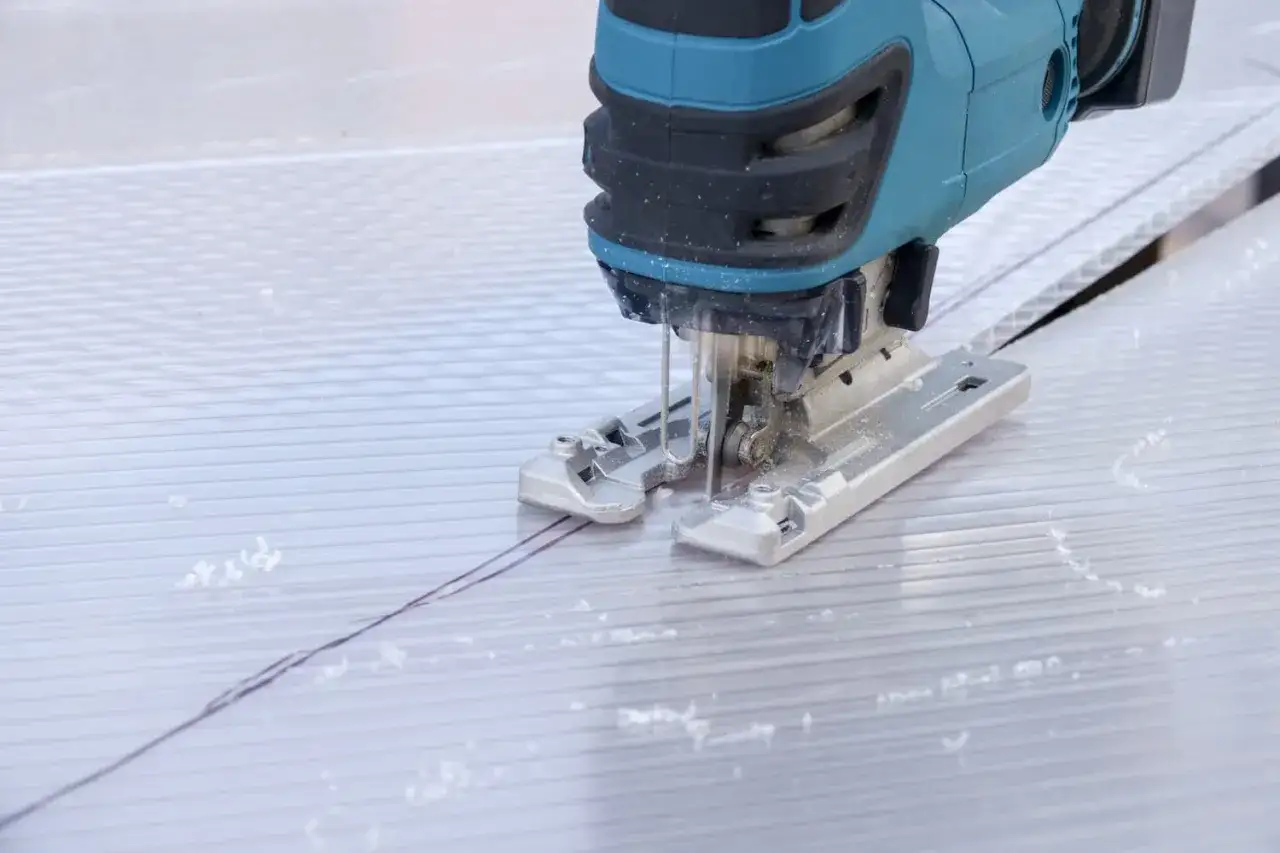 Mit einem Stichsägeblatt werden Hohlkammerplatten präzise geschnitten. Staubpartikel wirbeln auf, während die Säge entlang der Markierung gleitet.