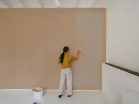 Frau streicht Wand neu. Man fragt sich, wie lange braucht wandfarbe zum trocknen, während sie die helle Farbe aufträgt.