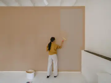Frau streicht Wand neu. Man fragt sich, wie lange braucht wandfarbe zum trocknen, während sie die helle Farbe aufträgt.